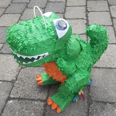 Green dinosaur piñata with big eyes and orange feet, shown as an inspiration reference
